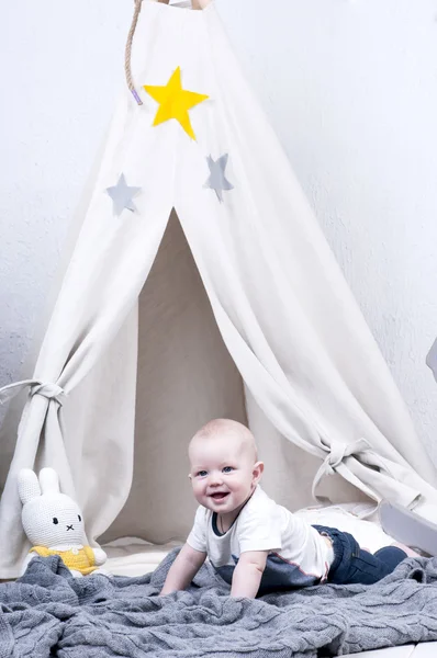 Cute baby creeps on gray knitted carpet near wigwam. — Stock Photo, Image
