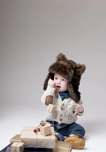 有趣的婴儿在冬季皮毛帽子与礼品盒在灰色背景 — 图库照片
