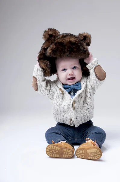 Funny baby boy in a winter fur hat cover gray background. — Stock Photo, Image