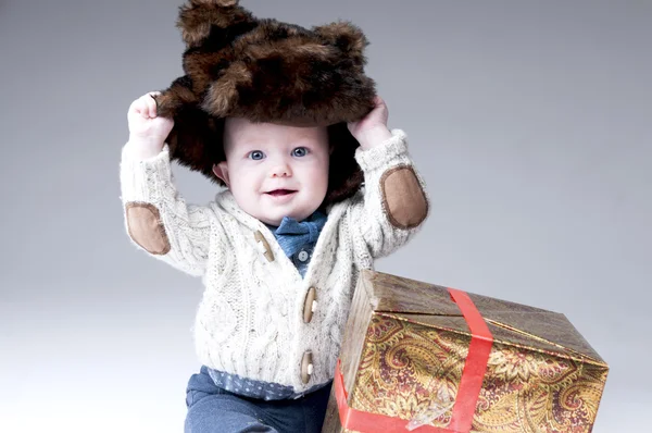 Funny baby boy i en vinter päls hatt med presentask. — Stockfoto