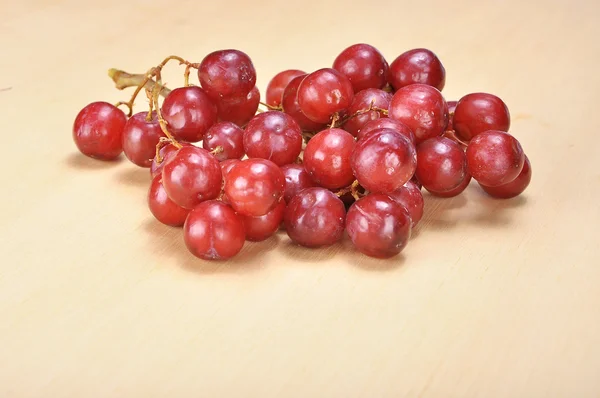 Delicioso cacho vermelho sem sementes de uva carmesim na prancha de madeira — Fotografia de Stock