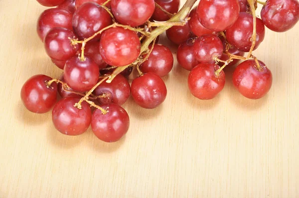 Delicioso cacho vermelho sem sementes de uva carmesim na prancha de madeira — Fotografia de Stock