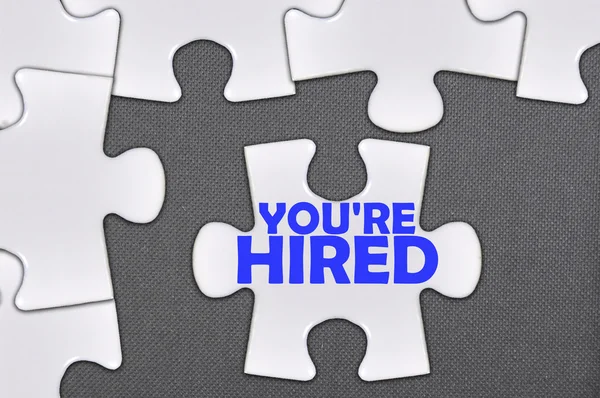 Jigsaw puzzle written word you're hired — Stock Photo, Image