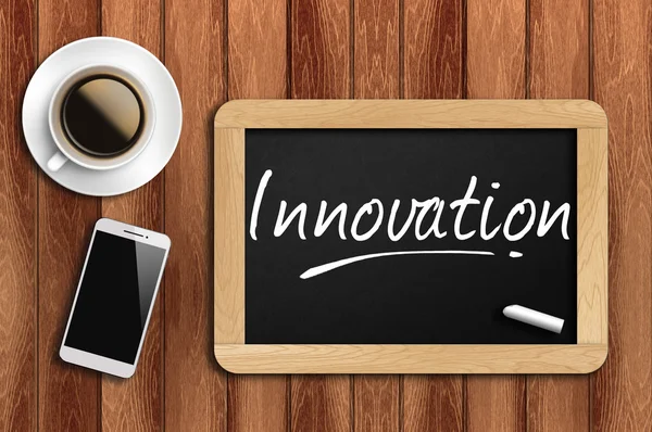 Café, telefone e quadro-negro com palavra inovação — Fotografia de Stock
