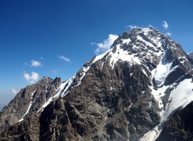 Bulutlu arkaplandaki karlı kaya dağının tepesinde