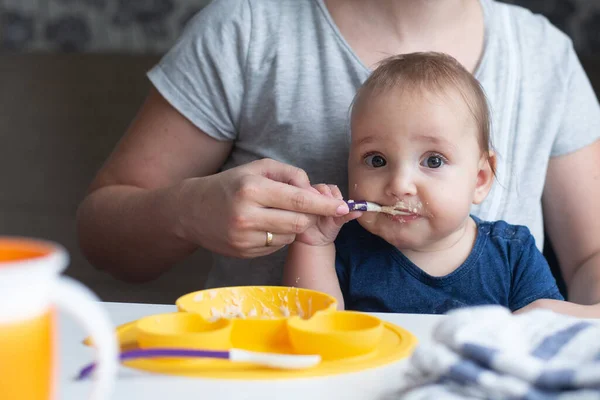 可爱的婴儿试图用勺子吃婴儿食品 而他快乐的母亲在他的帮助下 蓝色和灰色 — 图库照片