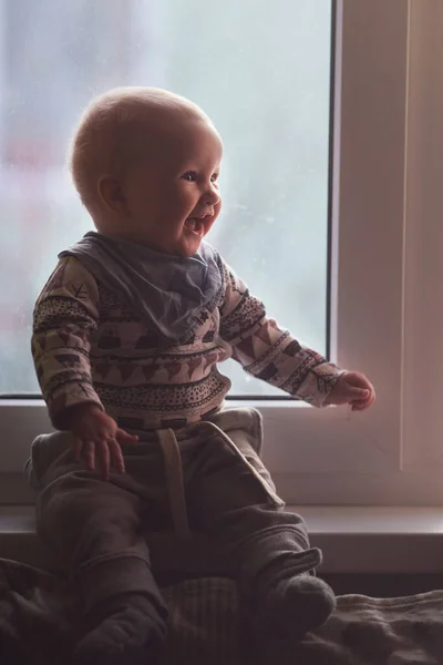 快乐的婴儿坐在窗台上笑着。冬日，平安夜 — 图库照片