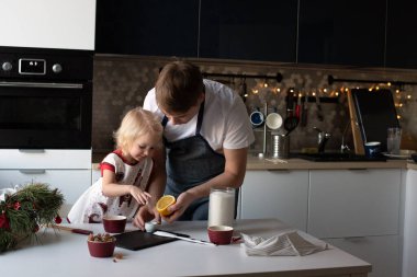 Genç baba ve küçük tatlı kızı birlikte Noel lolipopları yapıyorlar. Mutfak yeni yıl için dekore edildi..