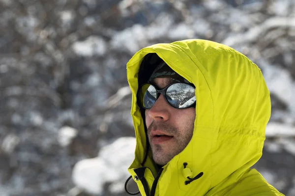 Portrait of young man in bright yellow jacket wearing mirror glasses with mountain reflection. Copy space