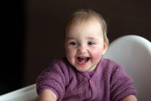 Mignon bébé rire insouciant assis sur une chaise de bébé. Bébé porte du lilas tricoté globalement. — Photo