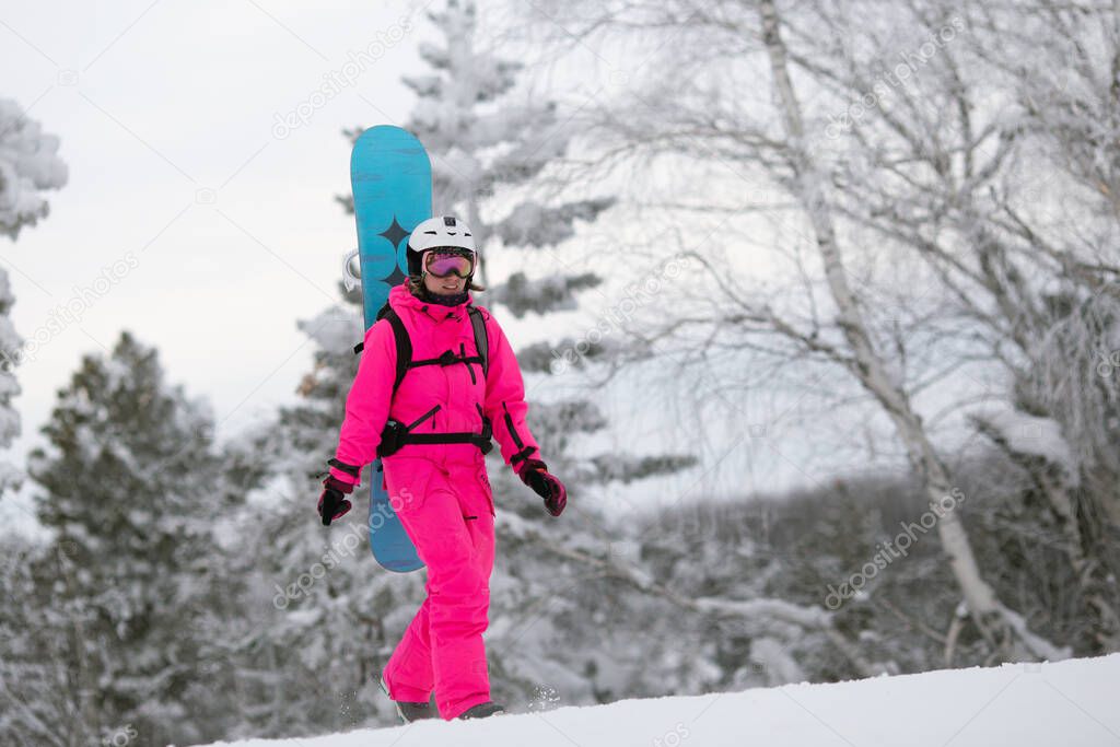 Woman in bright pink sportive overall with snowboard on the backpack having fun outisde in snowy day