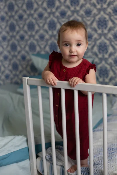 大红大紫的小女孩站在床边 看着镜头 蓝白相间的背景纵向方向 — 图库照片