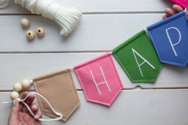 Evde işlemeli harflerle keçeli bayrak nasıl yapılır? Adım adım talimatlar. Eller DIY projesi yapıyor. Adım 8: Halat kullanarak bayraklardan çelenk yap. Bağlamak için döngü yapmayı unutma