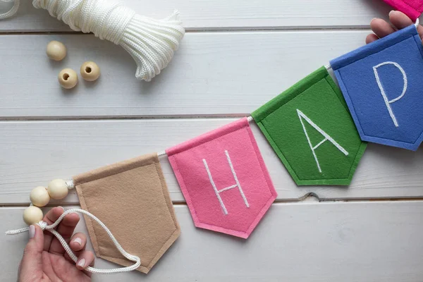 Evde işlemeli harflerle keçeli bayrak nasıl yapılır? Adım adım talimatlar. Eller DIY projesi yapıyor. Adım 8: Halat kullanarak bayraklardan çelenk yap. Bağlamak için döngü yapmayı unutma