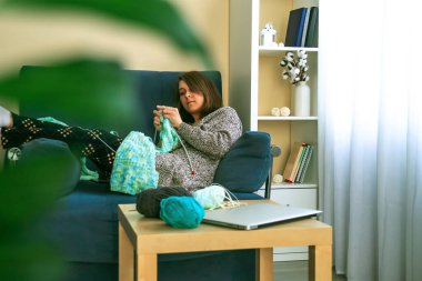 Evdeki kanepede oturan genç bir kadın örgü örüyor.