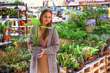 Çiçekçinin ortasında elinde canavarla elinde çömlek tutan genç bir kadın.. 