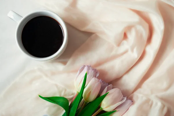 Lale buketi ve bir fincan kahve katlı ipek kumaşın arka planında yatıyor.. — Stok fotoğraf