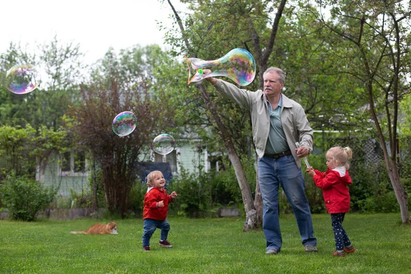 Homme âgé jouant avec ses petits-enfants dans le jardin. Grand-père fait des bulles de savon — Photo