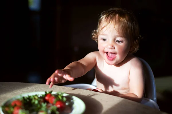 可爱的女婴在室内阳光下吃草莓 — 图库照片