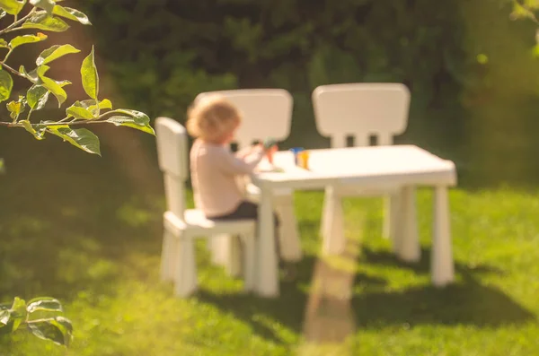 Fond d'été avec une image peu focalisée de petite fille jouant à une table. — Photo