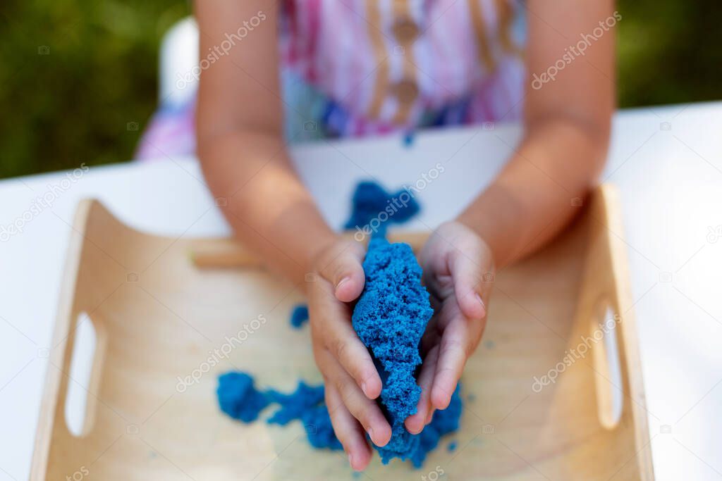 Hands of little girl playing with kinetic sand close-up. Leisure activity outdoors in summer day.