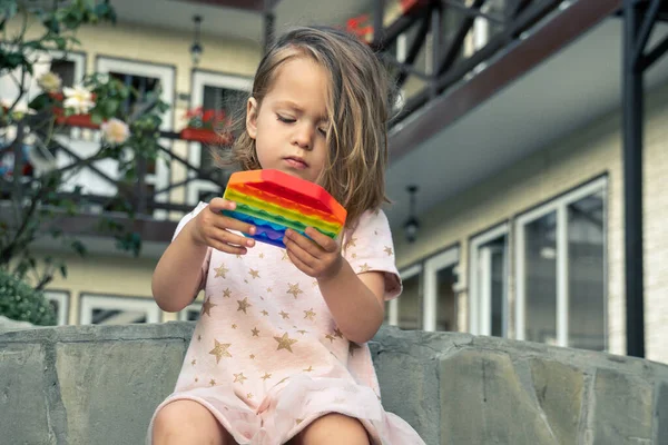 Retrato de niña linda concentrada jugando popit toy al aire libre, en el patio de una pequeña casa de huéspedes. — Foto de Stock