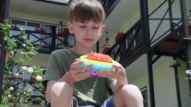 Retrato de menino sério e concentrado jogando popit brinquedo ao ar livre, no quintal de uma pequena casa de hóspedes. Fechar.. — Vídeo de Stock