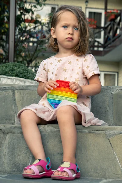 Retrato de niña linda concentrada jugando popit toy al aire libre, en el patio de una pequeña casa de huéspedes. — Foto de Stock