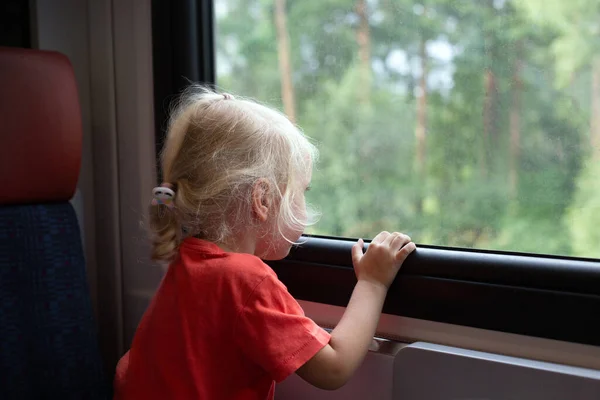 Little girl blonde hair travelling by train. Girl is looking through window. Public transportation — Foto de Stock