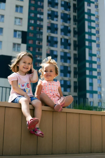 Deux jolies petites filles assises à l'extérieur dans un paysage urbain. Génération alpha. Format vertical, sœurs — Photo