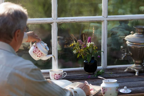 Yazın çaylı teras içerek kitap okuyan kıdemli adam. Kırsal eski pencere — Stok fotoğraf