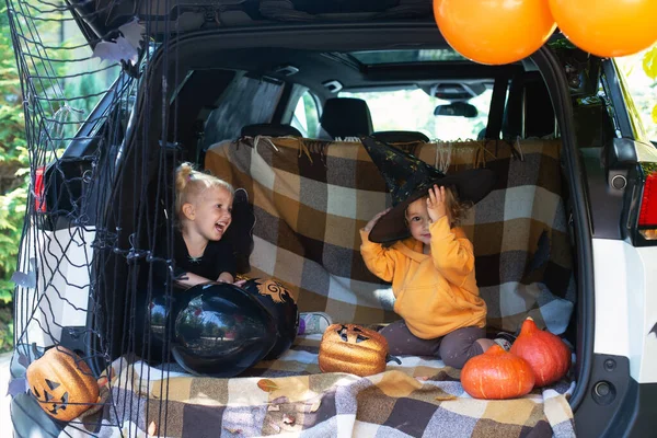Two little girls celebrating Halloween car trunk. Safe Autumn holidays