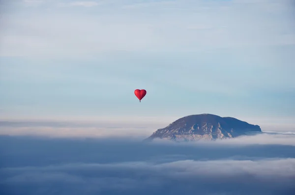 Globo de aire en forma de corazón volando sobre las nubes y mo —  Fotos de Stock