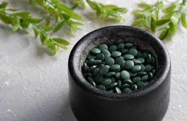 Klorella spirulina tabletlerinin gri bir zemin üzerinde, taştan bir havan topuna serpilmesi.
