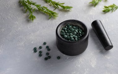Klorella spirulina tabletlerinin gri bir zemin üzerinde, taştan bir havan topuna serpilmesi.. 