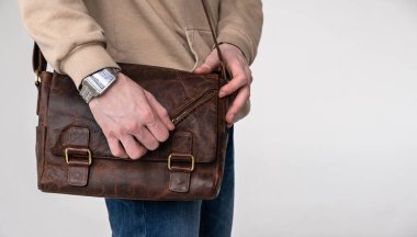 Açık arkaplanda kahverengi deri çantalı bir adam.