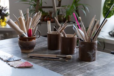 Masanın üzerinde fırçalı seramik bardaklar var.