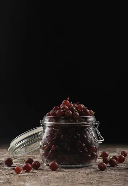 Gooseberry berries in a glass jar on a dark background — Stockfoto