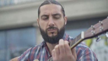 Açık havada gitar çalan Kafkasyalı müzisyenin yakın plan portresi. Şehir merkezinde performans sergileyen yakışıklı bir adam. Hobi ve yaşam tarzı.