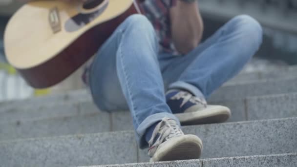 Voet van onherkenbare gitarist tikken ritme op stedelijke stadstrap. Man Kaukasische muzikant die buiten gitaar speelt. Kunstconcept. — Stockvideo