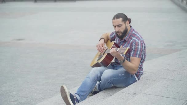 Top vinkel syn på allvarliga musiker som utför på urban stad trappor. Porträtt av stilig eftertänksam vit man som spelar gitarr utomhus på sommardagen. Musikkoncept. — Stockvideo