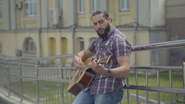 Porträtt av ung stackars gitarrist som uppträder i urban stad. Snygg vit manlig tiggare som spelar gitarr stående på gatan. Livsstilskoncept. — Stockvideo