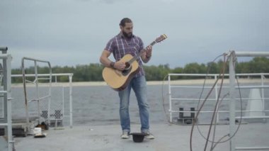 Kızgın müzisyenin geniş açılı çekimi gitar çalmayı ve bacağıyla şapkaya vurmayı bırakır. Mutsuz bir beyaz adamın portresi, şehir seti üzerinde performans sergiliyor. Dilencilik ve yoksulluk.