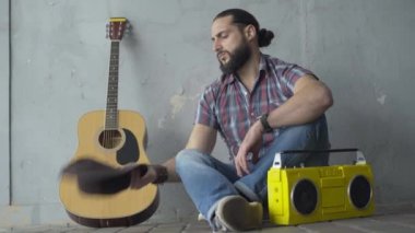 Depresyondaki adam yeraltı geçidinde oturuyor ve boş şapkayla bakıyor. Beyaz bir erkek dilencinin portresi. Açık havada gösteri yapacak parası yok. Gitar ve retro teyp yerde duruyor..