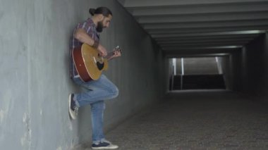 Yan bakış açısıyla, yeraltı geçidinde çalan beyaz gitaristin geniş açılı görüntüsü. Şehir merkezinde para için gösteri yapan özümsenmiş bir adam. Modern toplumda dilenmek.