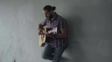 Yeraltı geçidinde gri duvara karşı duran ve gitar çalan özümsenmiş gitarist. Beyaz müzisyenin açık havada sergilediği portre. Sanat ve dilencilik konsepti.