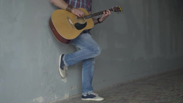 Unrecognizable street musician standing at wall in underground crossing and playing guitar. Male poor Caucasian beggar performing in urban city. Poverty concept. — Stock Video
