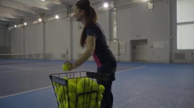 Canlı kamera, sporcu kadın sarı tenis topunu alıp servis ediyor. Spor oyunu oynayan iki profesyonel Kafkasyalı kadının olduğu kapalı bir tenis kortunun geniş açılı çekimi..