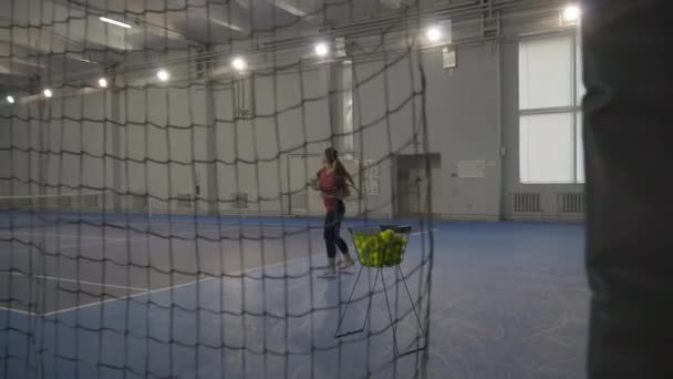 Extreem breed schot van sportvrouw slaan bal met tennisracket in de sportschool. Schieten achter net van zelfverzekerde blanke vrouw training binnen. Workout en gezonde levensstijl concept. — Stockvideo