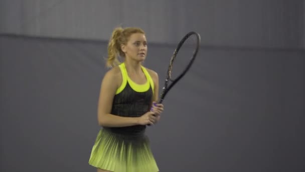 Live camera follows young slim sportswoman hitting ball with racket in gym. Confident serious Caucasian woman playing big tennis indoors. Workout and training concept. — Stock Video